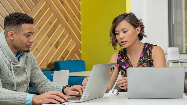 Man and woman sitting at a table looking at laptops.