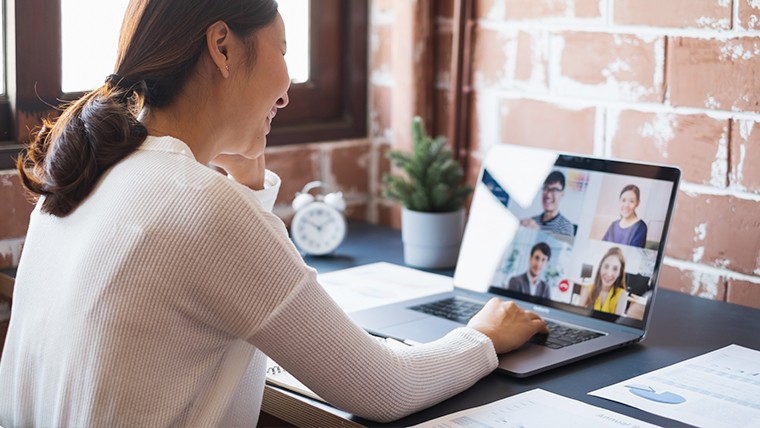 Woman sitting at a desk in a Zoom meeting on laptop.