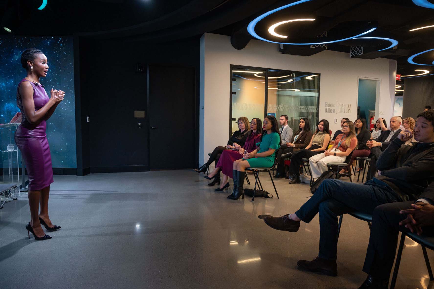 A group of people listening to a woman on stage at an event hosted by the Helix